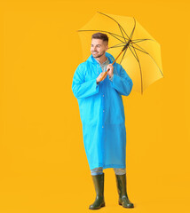 Young man in raincoat and with umbrella on color background