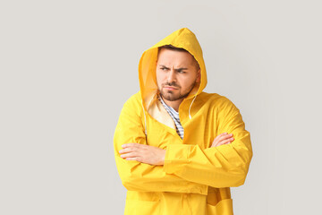 Displeased young man in raincoat on light background