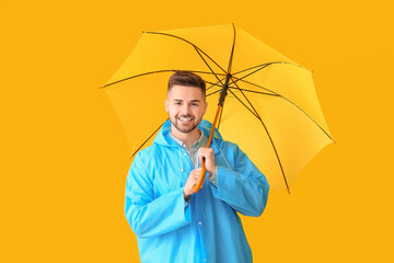 Young man in raincoat and with umbrella on color background