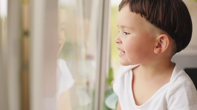 Little boy sitting on windowsill look at windows. Boy tell story or ask some question. Why phase. Boy stay at home and sitting near window.