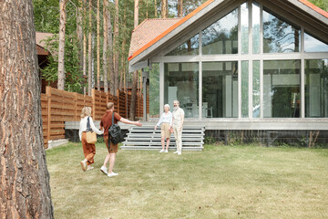 Senior parents standing against modern house and welcoming older kids after long separation