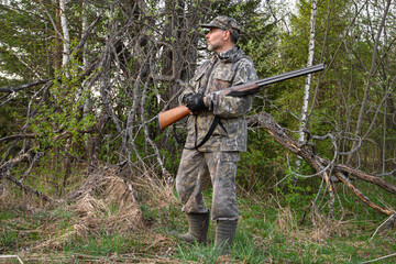 a hunter with a shotgun stands by a dead tree