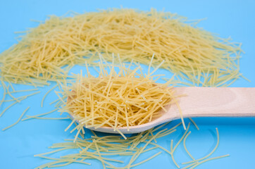 small uncooked pasta in a wooden spoon on a blue background.