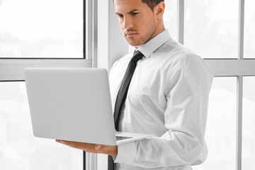 Young businessman in stylish shirt and with laptop near window in office