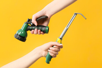 Female hands with water hose and rake for gardening on color background