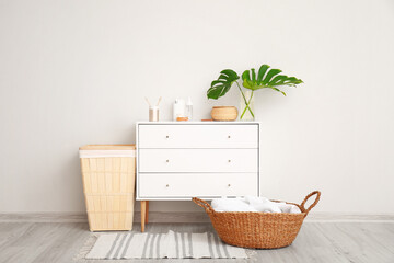 Baskets with towels and chest of drawers with cosmetics in bathroom