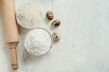 Bowls with rice, flour, eggs and rolling pin on white table