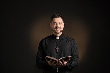 Handsome priest with Bible on dark background