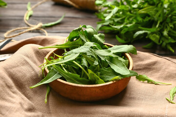 Bowl with fresh arugula on wooden background