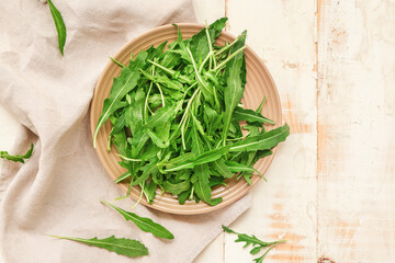 Plate with fresh arugula on wooden background