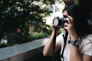 Asian woman sitting in a coffee shop taking a picture with a film camera