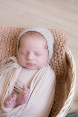 Cute little baby in a knitted hat with a toy bunny lies in a wicker basket  in a beige knitted blanket. Summer mood. Happy healthy childhood