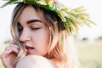 Naklejka premium Young, slender girl in a wreath of wheat ears at sunset in a field