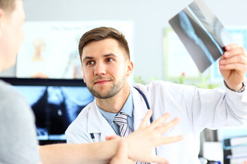 Fototapeta premium Portrait of smiling doctor talking with patient about good snapshot results. Doc looking at visitor with joyfulness. Medical and healthcare concept. Blurred background