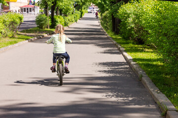 Little blonde girl riding a children's bike on the city sidewalk for a walk. 