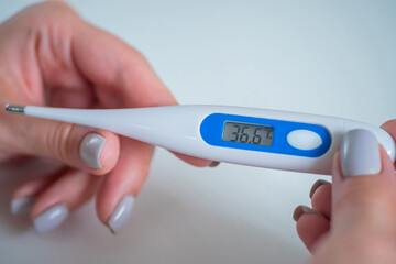 Woman hands showing digital medical thermometer with normal body temperature 36.6 - close up, selective focus. Healthcare, measurement, disease, covid 19, infection, coronavirus concept