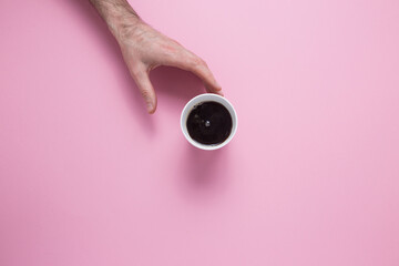 A male hand reaches for a glass with a coffee on a pink background. View from above.