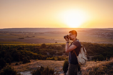 Man photographer with backpack and camera taking photo of sunset mountains