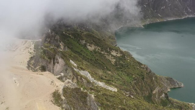 Aerial view of the Quilotoa lake in the crater of the vulcano showing the cliff descending down to the lake covered in clouds

