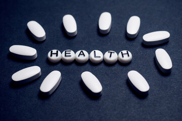 Health sign made from beads on a dark blue background with white pills around it, Health and medical treatment concept.