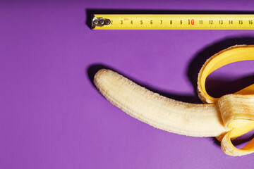 Yellow banana penis concept measured by measuring tape on pink background. Comparison of the size...