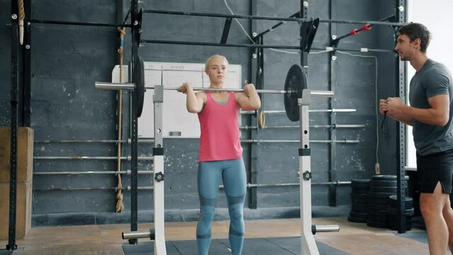 Pretty girl is lifting weight in gym while man trainer is motivating student talking gesturing enjoying personal training with woman. People and sports concept.