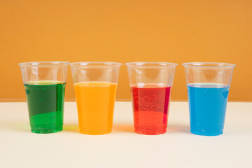 Sweet rainbow soda sparkling water in plastic cup with copy space. Green. Blue. Orange. Red.