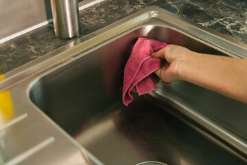 Woman maid hand cleaning sink with rag cloth in kitchen.