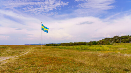 Swedish flag waving in wind with beautiful cloudy sky in the background on countryside in south Sweden. Swedish midsummer concept.