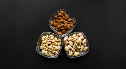 Almond, pistachio and cashew in a small plates which standing on a black table. Nuts is a healthy vegetarian protein and nutritious food.