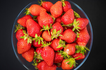 Fresh organic strawberries in  glass bowl  on  black table.