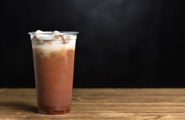 Iced coffee with ice and cream in a plastic glass on a black background with copy space
