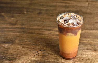 Plastic cup with coffee cocktail made from orange juice, caramel and ice on a wooden table with copy space