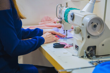 Fashion and tailoring concept. Professional tailor, fashion designer sitting and working at sewing studio, atelier. Close up side view of woman hands using retro sewing machine