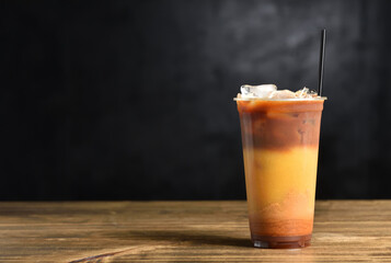 Summer drink made from orange juice, caramel, ice and coffee in a plastic glass with a straw