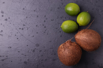 brown coconuts and citrus (green limes) on stone dark grey surface. minimalism. top view.