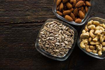 Almond, sunflower seeds and cashew in a small plates which standing on a vintage wooden table. Nuts is a healthy vegetarian protein and nutritious food.