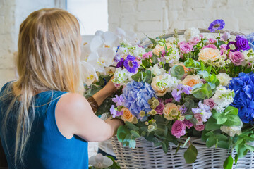 Professional woman floral artist, florist making large floral basket with flowers at workshop, flower shop. Floristry, handmade, wedding, birthday, holiday and small business concept