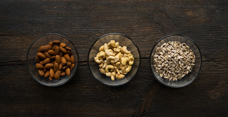 Fototapeta na wymiar Almond, cashew and sunflower seeds in a small plates which standing on a vintage wooden table. Nuts is a healthy vegetarian protein and nutritious food.
