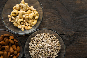 Almond, cashew and sunflower seeds in a small plates which standing on a vintage wooden table. Nuts is a healthy vegetarian protein and nutritious food.