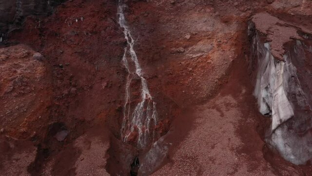 A waterfall of meltwater next to the last remnants of a large ice or snow wall of a glacier
