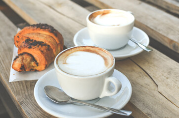 Two cups of cappuccino with latte and croissant on wooden background. stylish toning. morning coffee for couple in love.