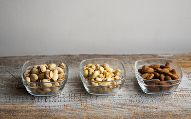 Almond, pistachio and cashew in a small plates which standing on a vintage white table. Nuts is a healthy vegetarian protein and nutritious food.
