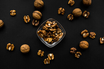 Obraz na płótnie Canvas Walnut in a small plate with scattered shelled nuts which standing on a black surface. Walnuts is a healthy vegetarian protein nutritious food.