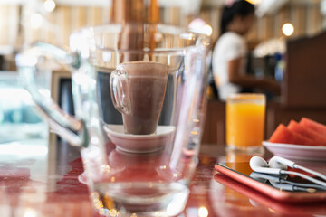 Cup of coffee through a transparent glass cup, smartphone with headphones, freshly squeezed cold orange juice and plate with slices of watermelon on a cafe table