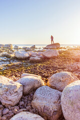 Fototapeta na wymiar man stands on a stony coastline at dawn inspiring by life freedom concept