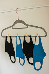 Photo of some reusable face masks colour blue and black hanging on a cloth rack while drying after washing. White background inside a house. Coronavirus outbreak