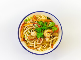 Udon noodles with seafood in a plate on a white surface. With vegetables greens