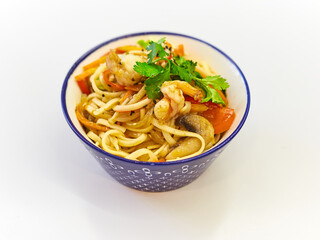 Udon noodles with seafood in a plate on a white surface. With vegetables greens