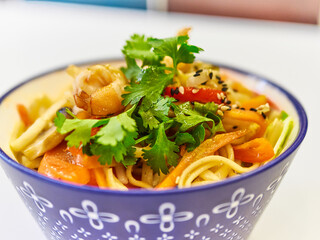 Udon noodles with seafood in a plate on a white surface. With vegetables greens